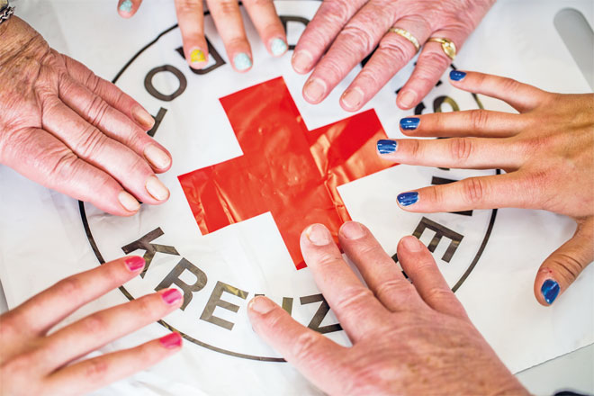 Foto: Sechs Menschen halten jeweils eine Hand über das große DRK-Logo.