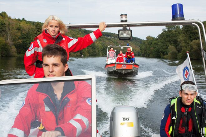 Foto: Zu sehen sind zwei Boote der BRK-Wasserwacht in voller Fahrt. Auf jedem Boot befinden sich jeweils drei BRK-Einsatzkräfte, einer trägt eine Taucherausrüstung.